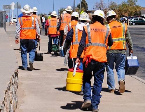 Line of construction laborers in hard hats and orange vests heading to a job site